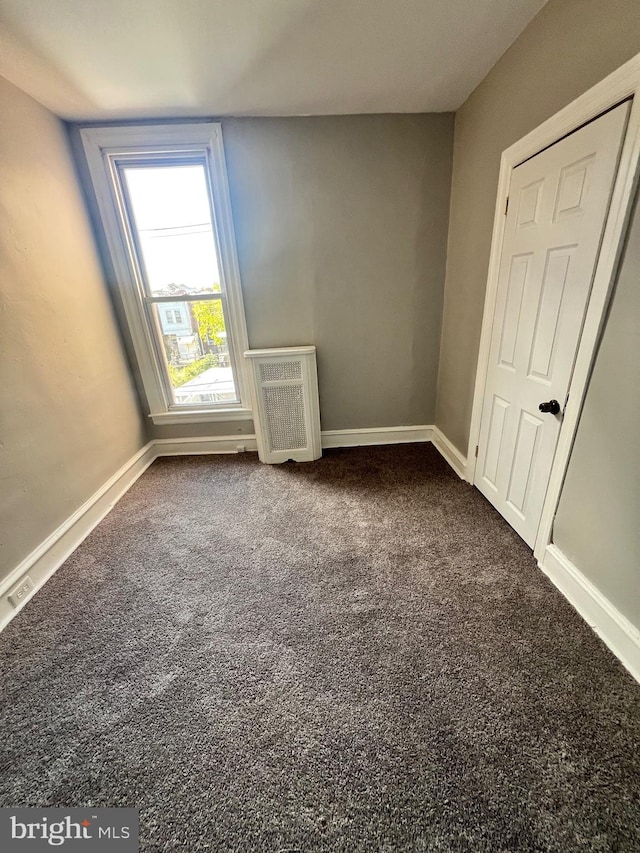 unfurnished bedroom with dark colored carpet and radiator heating unit