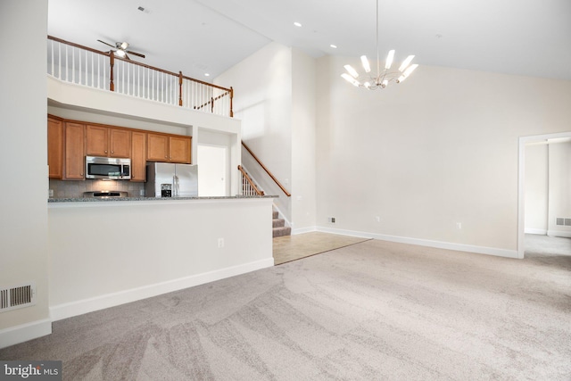 unfurnished living room featuring ceiling fan with notable chandelier, light carpet, and high vaulted ceiling