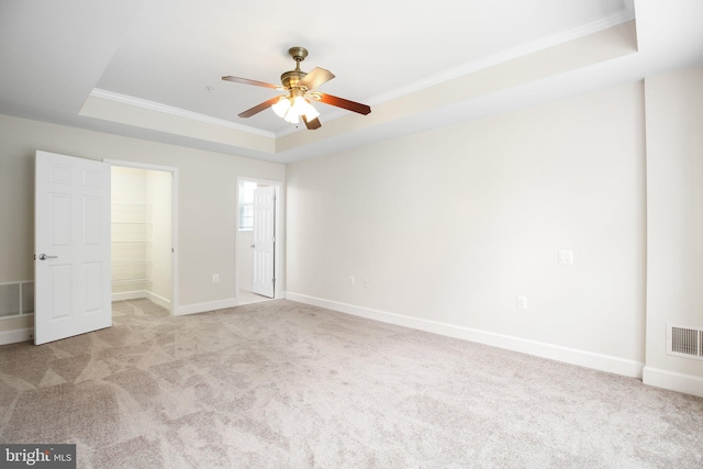 unfurnished bedroom with ornamental molding, ceiling fan, a raised ceiling, a walk in closet, and light colored carpet