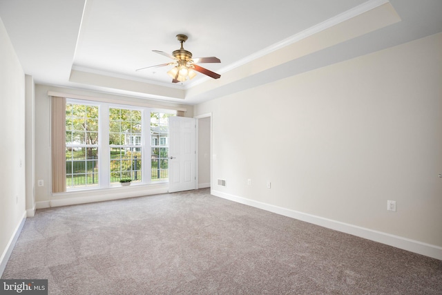 empty room with ceiling fan, ornamental molding, carpet flooring, and a tray ceiling