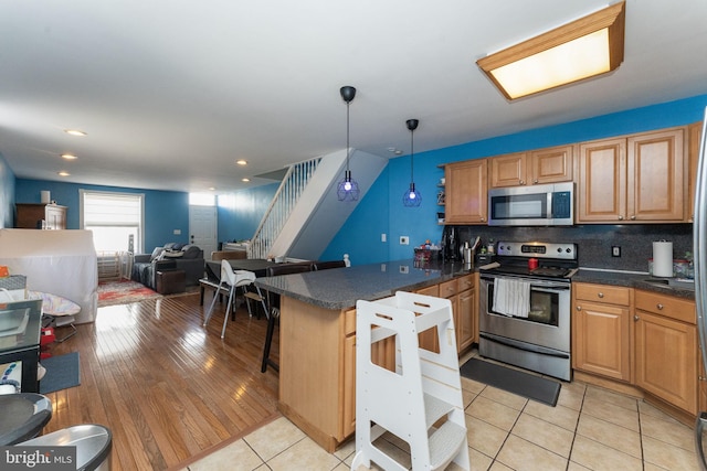 kitchen featuring kitchen peninsula, hanging light fixtures, stainless steel appliances, light wood-type flooring, and tasteful backsplash