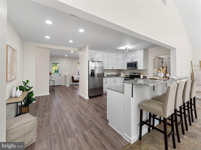 kitchen featuring stainless steel appliances, a kitchen breakfast bar, light stone counters, wood-type flooring, and white cabinets