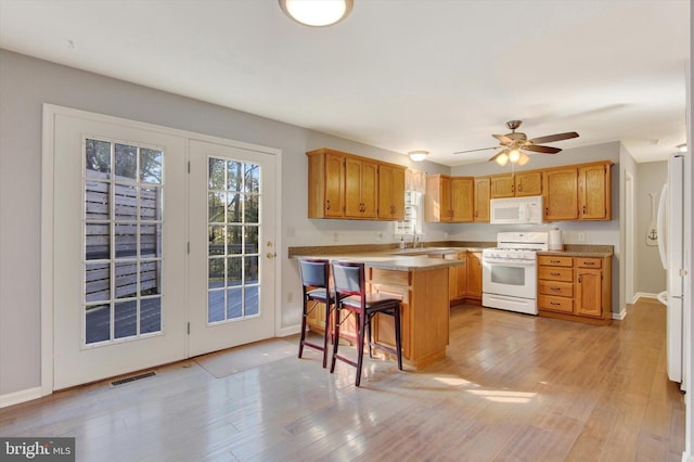 kitchen with ceiling fan, a breakfast bar, white appliances, kitchen peninsula, and light hardwood / wood-style flooring