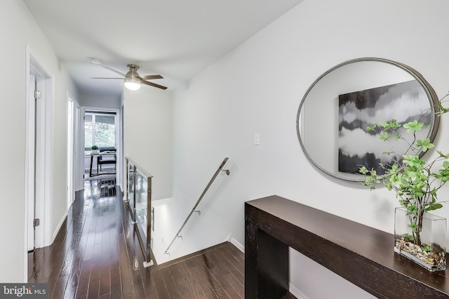 hallway with dark wood-style floors, baseboards, and an upstairs landing