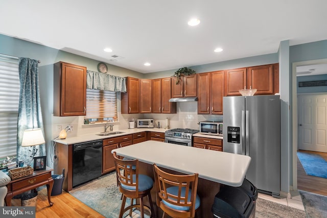 kitchen with appliances with stainless steel finishes, a kitchen bar, light hardwood / wood-style flooring, sink, and a center island