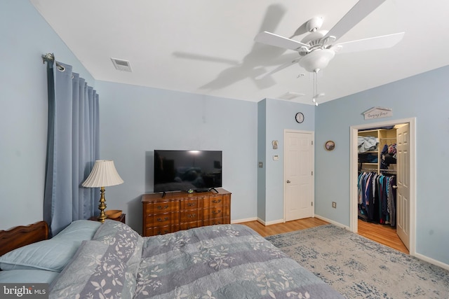 bedroom with a closet, a spacious closet, light wood-type flooring, and ceiling fan