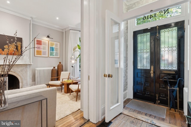 foyer entrance with visible vents, hardwood / wood-style flooring, radiator heating unit, and ornamental molding