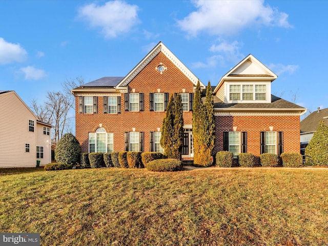 colonial-style house featuring solar panels and a front lawn