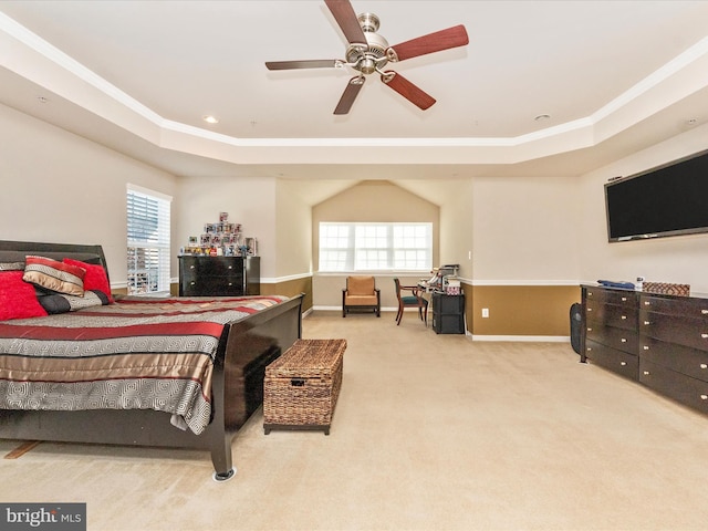 carpeted bedroom with a raised ceiling, multiple windows, ceiling fan, and ornamental molding