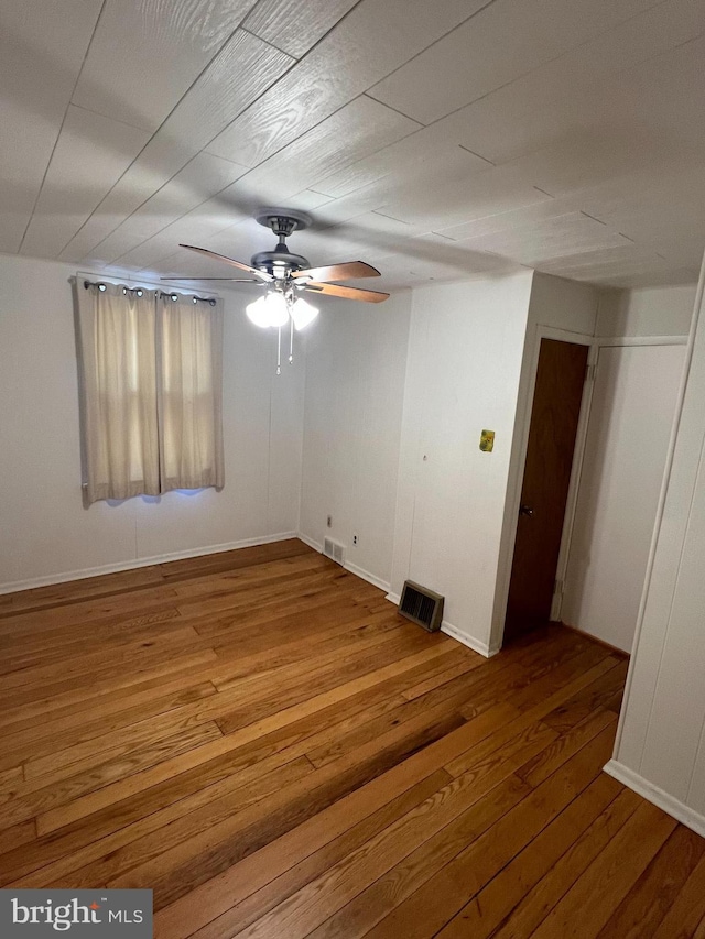 spare room with wood-type flooring, visible vents, and a ceiling fan