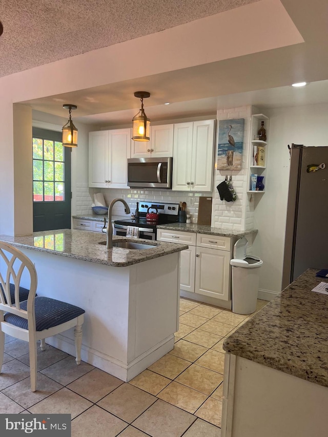 kitchen featuring hanging light fixtures, stainless steel appliances, white cabinets, light stone counters, and light tile patterned floors