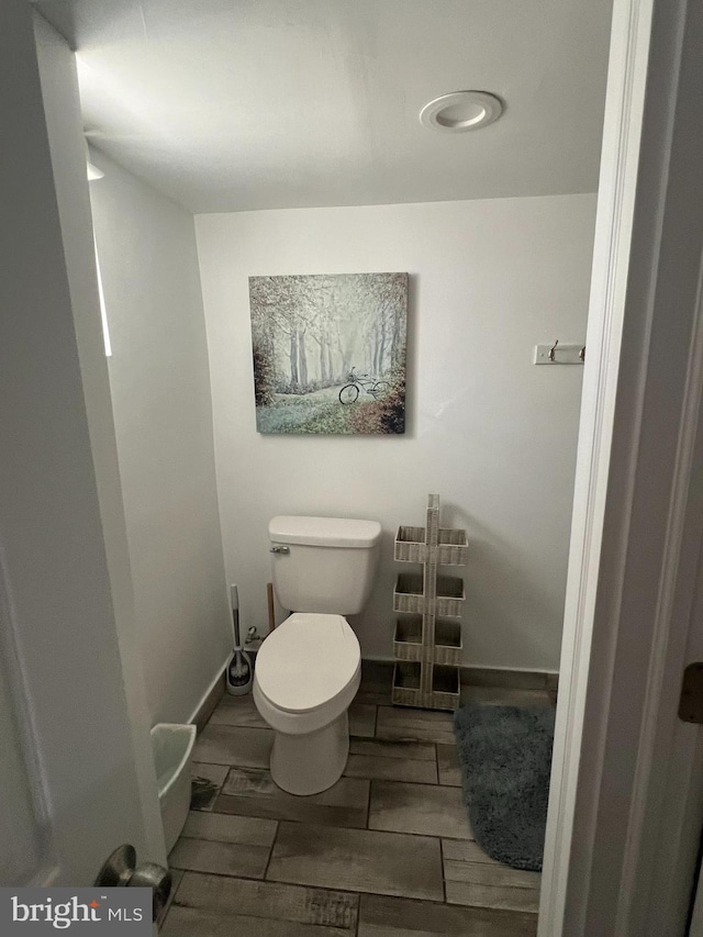bathroom with toilet, wood finish floors, and baseboards