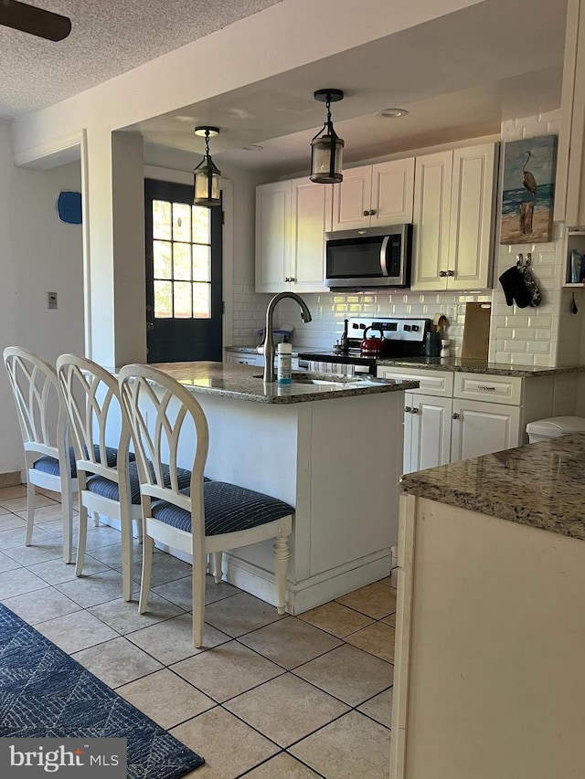 kitchen featuring stainless steel appliances, a sink, dark stone countertops, tasteful backsplash, and white cabinetry