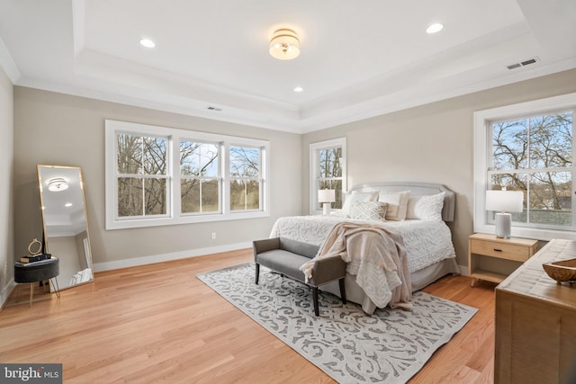 bedroom with a raised ceiling, multiple windows, and light hardwood / wood-style flooring