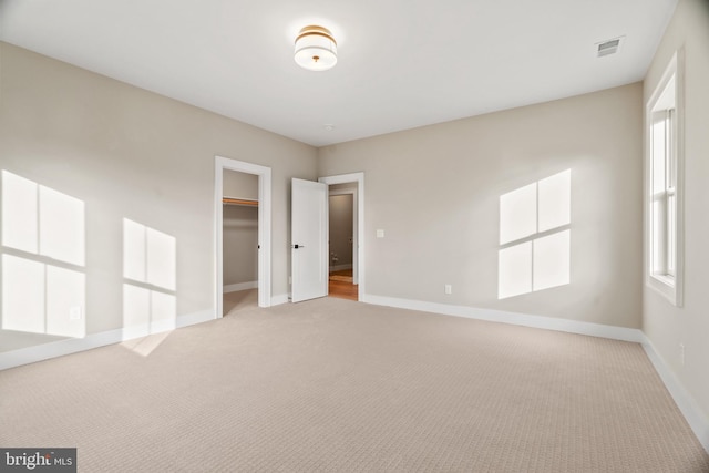 unfurnished bedroom featuring light carpet, a walk in closet, and a closet