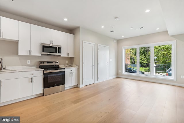 kitchen with sink, appliances with stainless steel finishes, white cabinetry, and light hardwood / wood-style floors