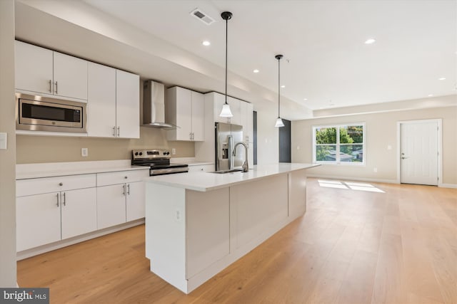 kitchen with white cabinetry, stainless steel appliances, wall chimney exhaust hood, decorative light fixtures, and a kitchen island with sink