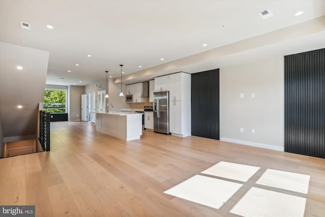 kitchen with appliances with stainless steel finishes, white cabinetry, decorative light fixtures, light hardwood / wood-style flooring, and a kitchen island with sink