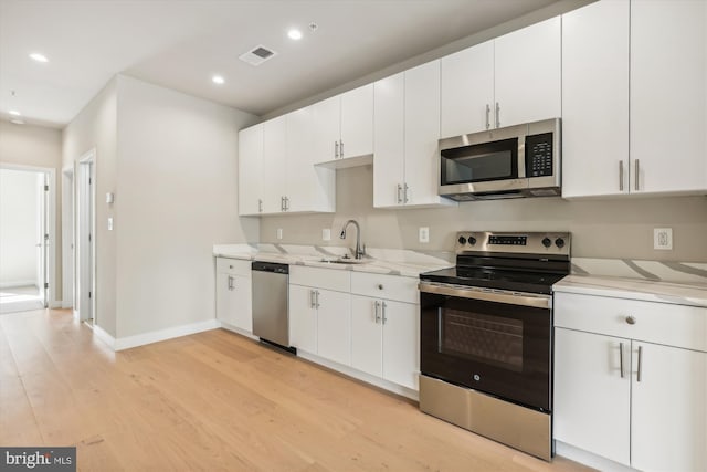 kitchen featuring sink, white cabinetry, light wood-type flooring, appliances with stainless steel finishes, and light stone counters