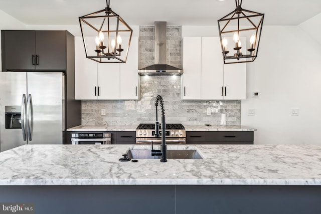 kitchen with hanging light fixtures, wall chimney exhaust hood, white cabinetry, and stainless steel appliances