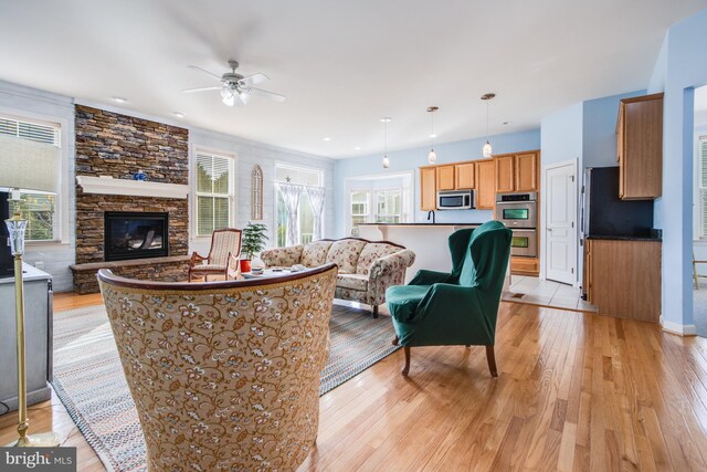 living room featuring ceiling fan, a stone fireplace, light hardwood / wood-style flooring, and plenty of natural light