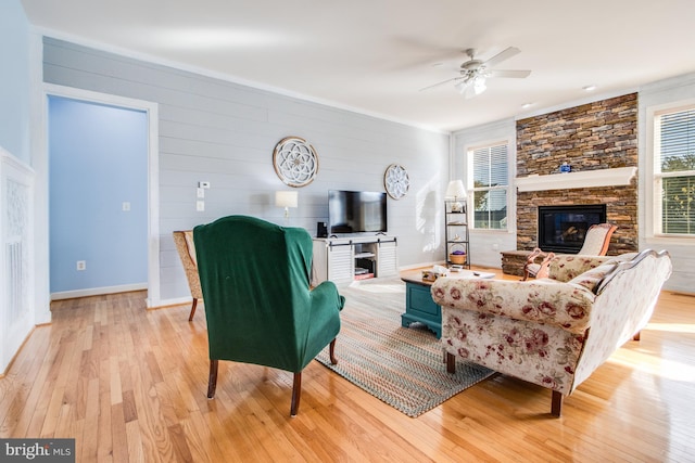living area with wooden walls, light wood-style flooring, a ceiling fan, and a fireplace