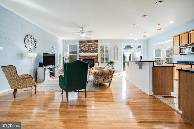 living room featuring a stone fireplace, light hardwood / wood-style flooring, sink, and ceiling fan