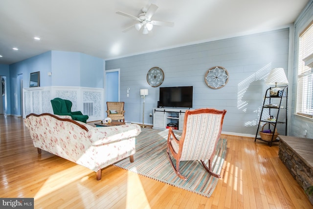 living room featuring a ceiling fan, recessed lighting, baseboards, wood-type flooring, and wooden walls