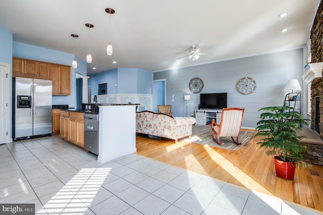 kitchen with a stone fireplace, decorative light fixtures, light wood-type flooring, appliances with stainless steel finishes, and ceiling fan