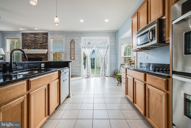 kitchen featuring light tile patterned floors, a sink, dark stone counters, stainless steel appliances, and a fireplace