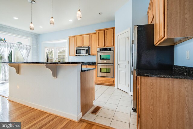 kitchen with pendant lighting, stainless steel appliances, dark stone counters, and light wood-type flooring