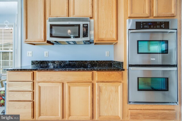 kitchen with stainless steel appliances, dark stone counters, and light brown cabinets