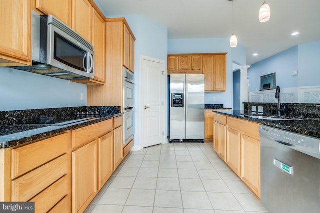 kitchen featuring light tile patterned floors, a sink, dark stone counters, decorative light fixtures, and appliances with stainless steel finishes