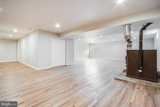basement featuring light wood-style floors, a wood stove, baseboards, and recessed lighting