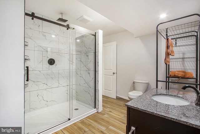 full bathroom featuring toilet, wood finished floors, vanity, a marble finish shower, and baseboards