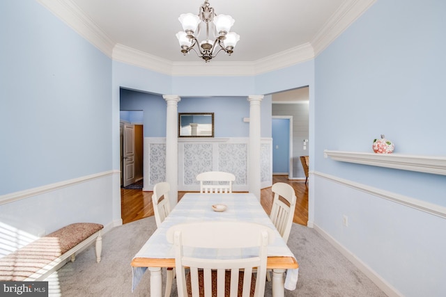 dining space featuring carpet, ornamental molding, a chandelier, and decorative columns