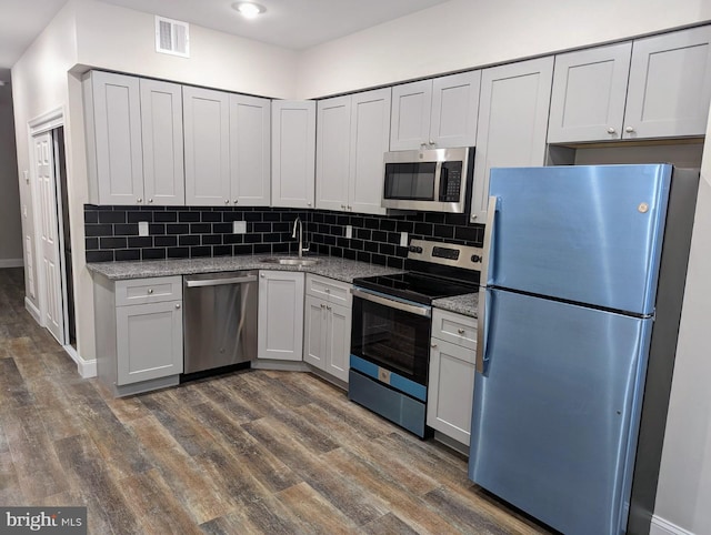 kitchen with sink, backsplash, stainless steel appliances, light stone counters, and dark hardwood / wood-style floors