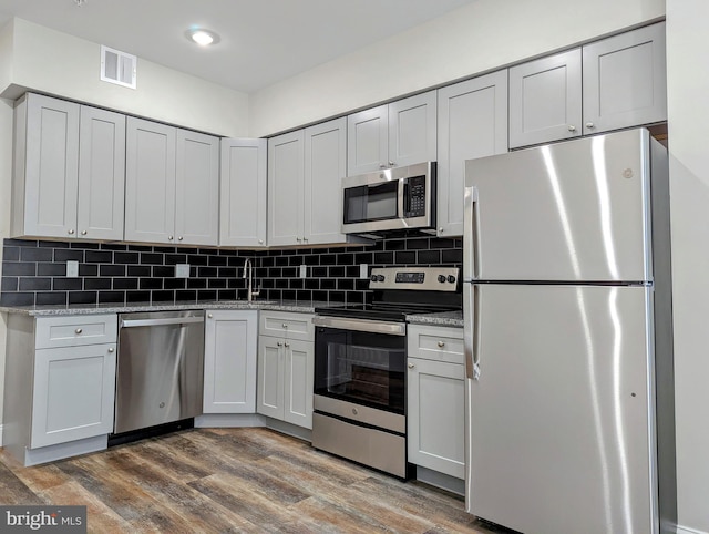 kitchen with hardwood / wood-style flooring, stainless steel appliances, tasteful backsplash, and light stone counters