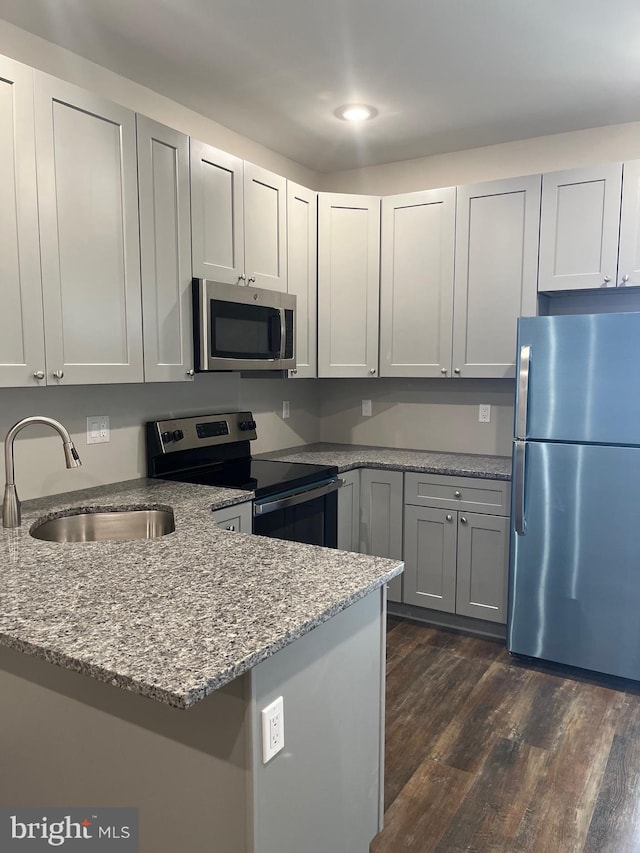 kitchen featuring kitchen peninsula, light stone counters, dark hardwood / wood-style floors, sink, and stainless steel appliances