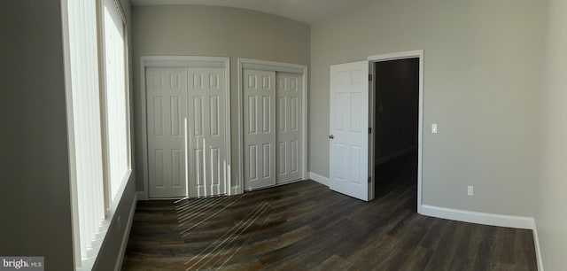 unfurnished bedroom with two closets and dark hardwood / wood-style floors