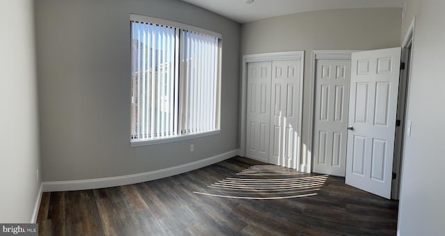 unfurnished bedroom featuring two closets, multiple windows, and dark hardwood / wood-style floors