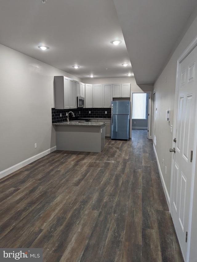 kitchen featuring appliances with stainless steel finishes, kitchen peninsula, dark hardwood / wood-style flooring, and backsplash