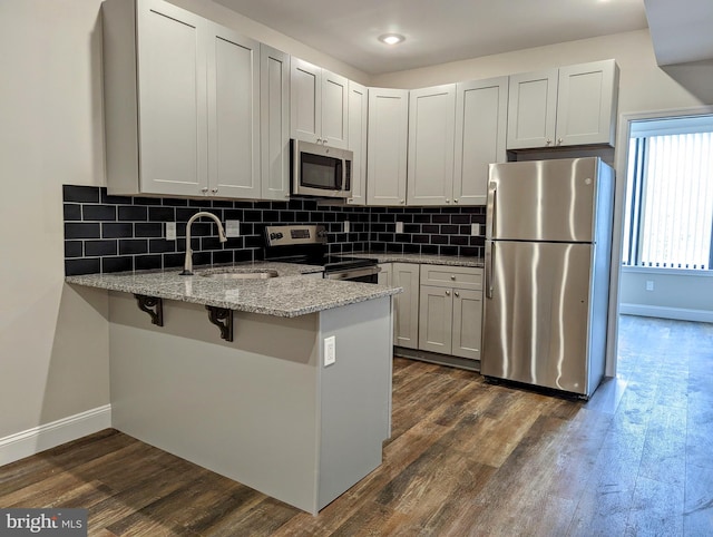 kitchen with dark wood-type flooring, kitchen peninsula, sink, appliances with stainless steel finishes, and light stone counters