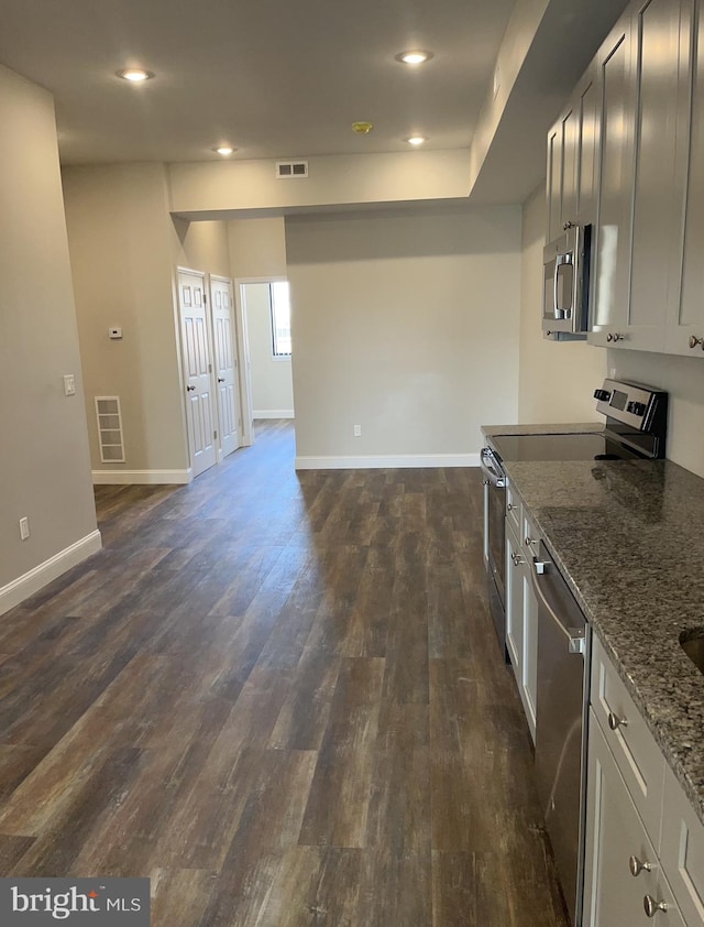 kitchen with gray cabinets, dark wood-type flooring, appliances with stainless steel finishes, and dark stone countertops