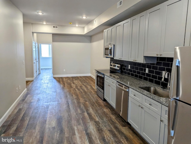 kitchen featuring sink, dark hardwood / wood-style flooring, white cabinetry, stainless steel appliances, and dark stone counters