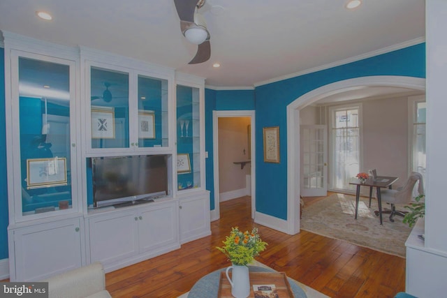 living area featuring arched walkways, hardwood / wood-style flooring, crown molding, and baseboards