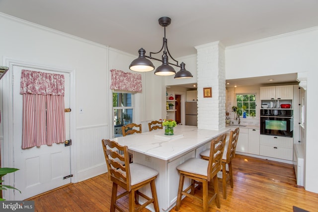 dining area with wainscoting, light wood-style floors, a wealth of natural light, ornamental molding, and ornate columns