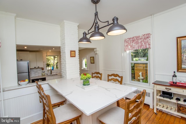 dining area with crown molding, light wood finished floors, ornate columns, and wainscoting