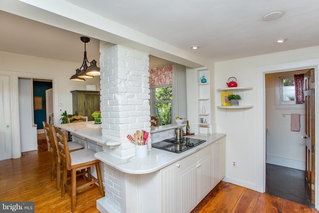 kitchen with black electric cooktop, ornate columns, light stone counters, wood-type flooring, and white cabinetry