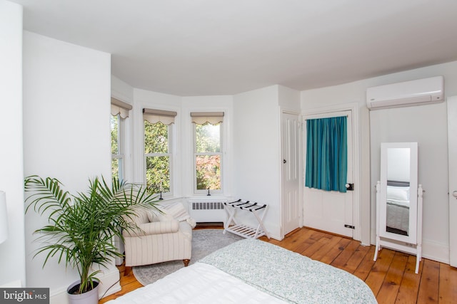 bedroom featuring radiator heating unit, a wall mounted air conditioner, hardwood / wood-style floors, and baseboards
